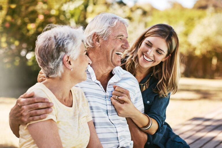 Family, senior parents and woman holding with care, love and hug bonding outdoor in a park. Smile, happy person and people in retirement with adult daughter together with bokeh in nature in summer.